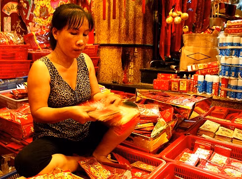 A local shop owner is counting a pack of red envelopes, which are printed with a yellow “Loc” (or Fortune) word 