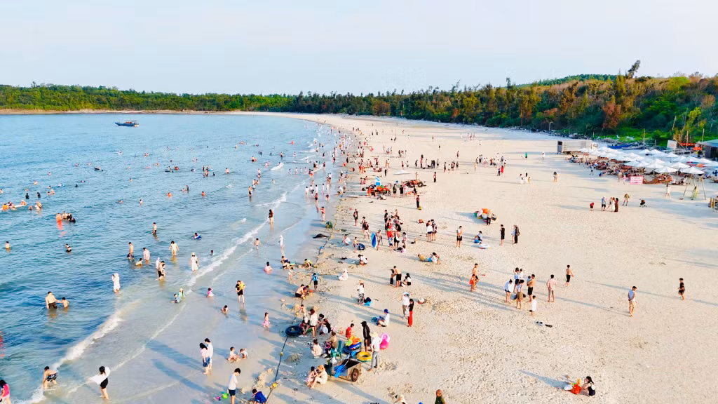 Minh Chau Beach is crowded with visitors swimming and enjoying seaside activities.