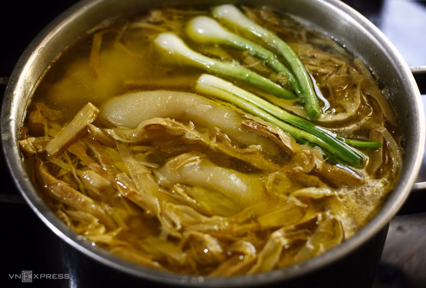 The simmering of pork knuckles with bamboo shoots infuses the dish with a golden tint. Photo by VnExpress/Bui Thuy