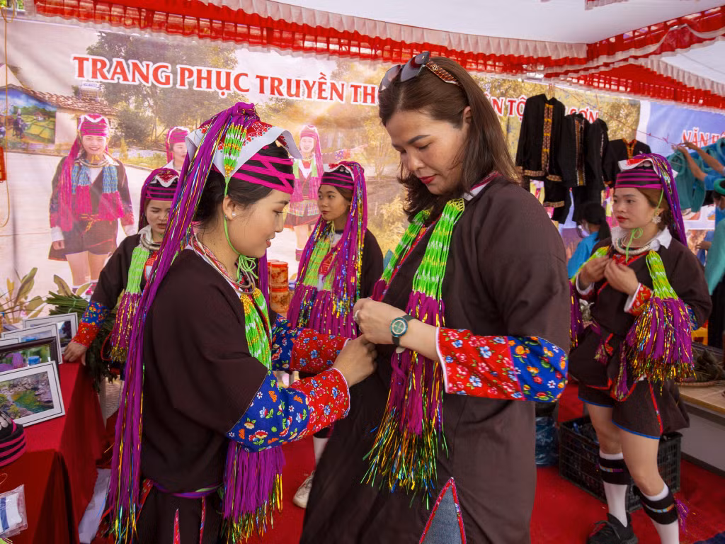 Ảnh 7: Phùn Thị Tâm đang giới thiệu trang phục Dao Thanh Y cho du khách trong hội chợ.