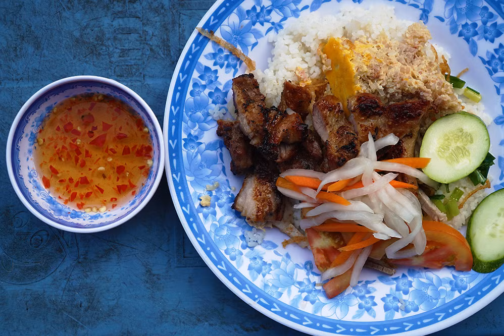 A plate of broken rice topped with grilled pork, egg meatloaf, cucumber slices and pickle. Photo by VnExpress/Di Vy