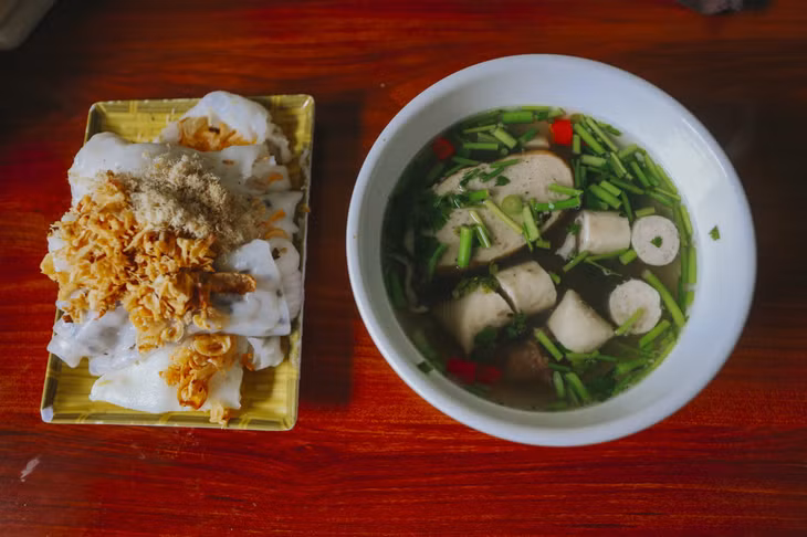 Rice rolls topped with pork floss and fried onions are served with a bowl of hot broth that contains sausages, herbs and chili. Photo by VnExpress/Xuan Phuong