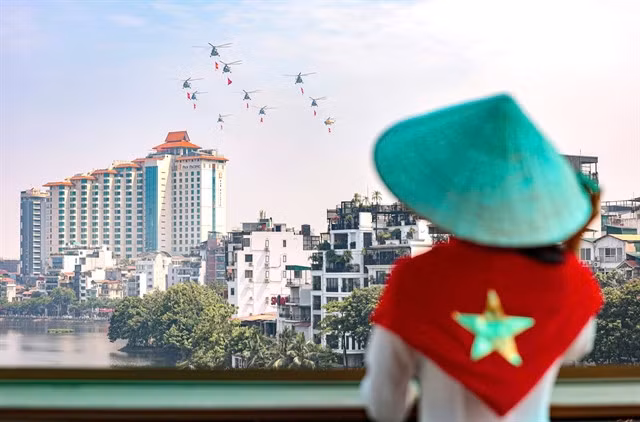 A Hà Nội resident watch helicopters carrying the Party flag and the national flag during a rehearsal in the city’s skies for the celebration of the 80th anniversary of Việt Nam's August Revolution and National Day. — VNA/VNS Photo