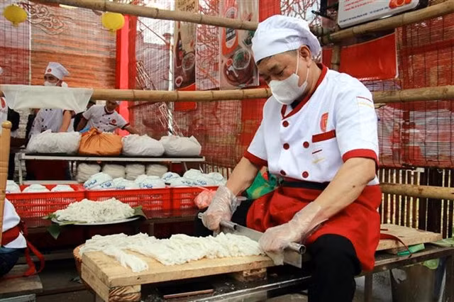 A chef cuts a large sheet of noodle into long thin strips. The noodles then will combine with other ingredients to make a delcious phở bowl.