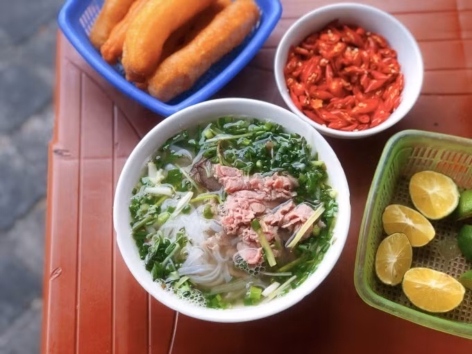 A bowl of beef pho, served alongside fried doughs, lime wedges, and chilies. Photo by VnExpress/Quynh Mai