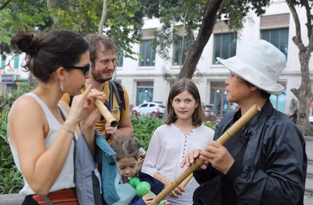 Foreign tourists try out the bamboo flutes as part of a cultural activity held in the pedestrian space Hoàn Kiếm, Hà Nội. — VNA/VNS Photo