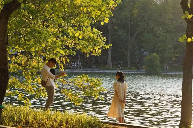 Two visitors take photos by Hoàn Kiếm Lake in autumn. VNA/VNS Photo