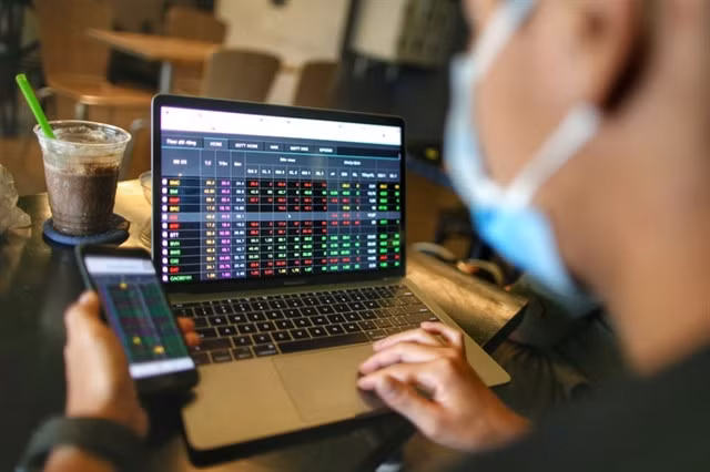 An investor watching stock movements on his smartphone and laptop. Photo nld.com.vn