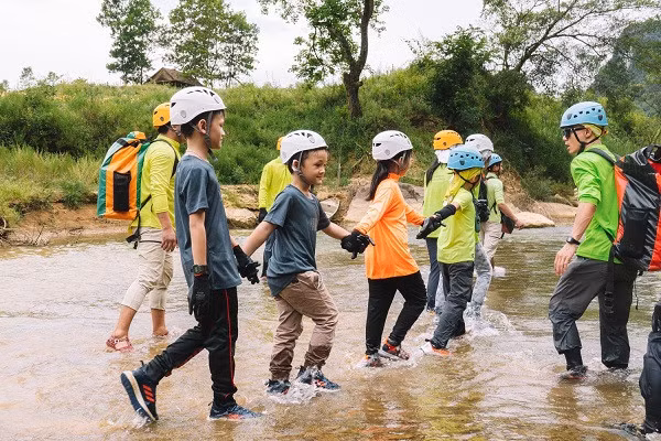 Children holding hands to cross Rao Nan river as part of their deep jungle expedition at Phong Nha – Ke Bang National Park in Quang Binh province (Photo: oxalisadventure.com)