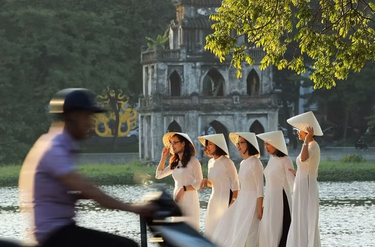 Girls in white ‘ao dai’ (traditional long dress) pose for a group photo at Hoan Kiem Lake, with the ‘Thap Rua’ (Turtle Tower) in the background. (Photo: VNA)