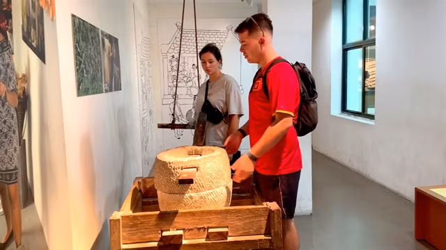 Two visitors learn how to use a stone mill at the Women's Museum. VNS Photo Lê Hương