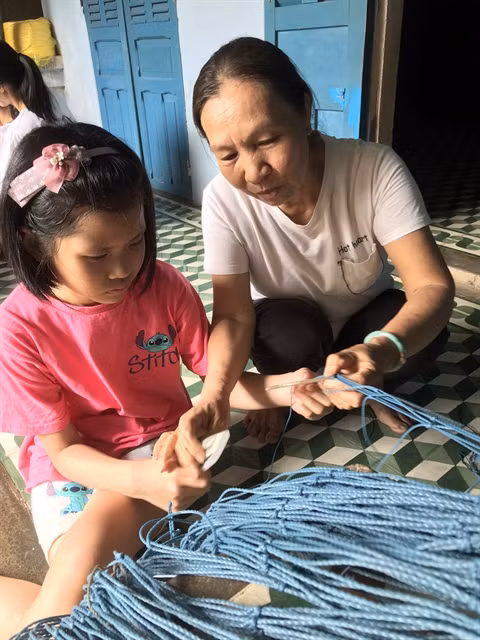 NEXT GENERATION: A girl learns how to make a fishing net at a home-stay service at Tân Diêm Village in the Sa Huỳnh salt fields. Photo courtesy of SAHU